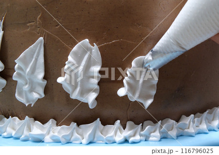 A woman pastry chef with a pastry bag in her hands squeezes cream on a cake in a home kitchen. Professional chef at work on bakery kitchen. culinary, baking and cooking food concept, home cooking 116796025