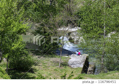 two people sitting on a rock at the edge of a stream two people sitting on a rock at the edge of a stream 116796451