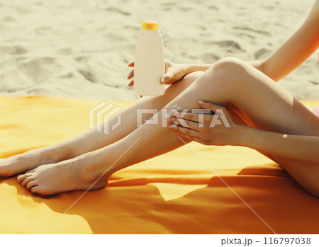 Summer vacation, woman sunbathing and applying suntan cream on her legs lying on sand on the beach Summer vacation, woman sunbathing and applying suntan cream on her legs lying on sand on the beach 116797038