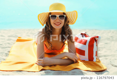 Summer vacation, happy smiling young woman with bag in hat lying on the sand on the beach on sea 116797043