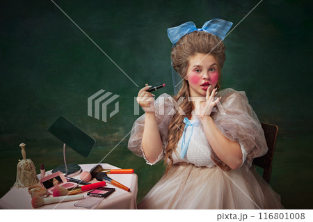 Fashion blog. Portrait of young woman with bright makeup look, applying lip gloss, against vintage green background 116801008