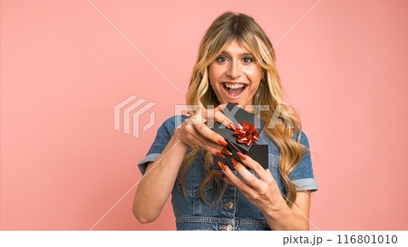 Happy transgender woman offering small gift box against pink background Happy transgender woman offering small gift box against pink background 116801010