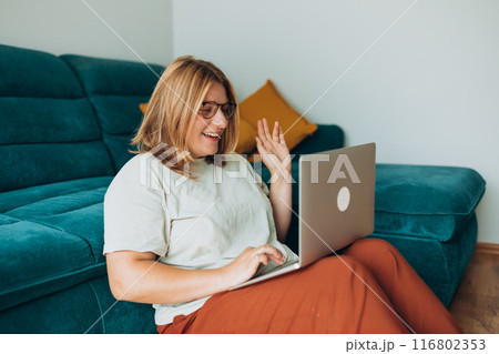 Nice beautiful woman in glasses working at the notebook near the sofa at home. Concepts of education, work and comfort. 30s female working indoors. Hello Nice beautiful woman in glasses working at the notebook near the sofa at home. Concepts of education, work and comfort. 30s female working indoors. Hello 116802353
