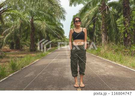 Woman in cargo pants and tank-top in tropical palm farm. Woman in cargo pants and tank-top in tropical palm farm. 116804747