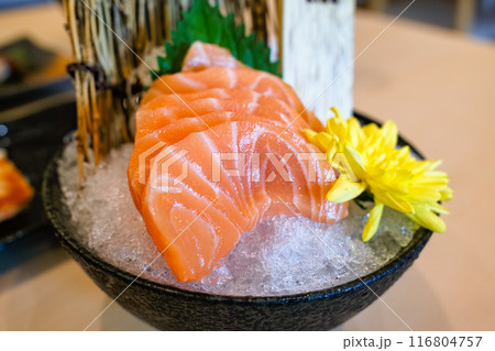 Ceramic bowl of sliced salmon sushi with yellow flower on crushed ice 116804757