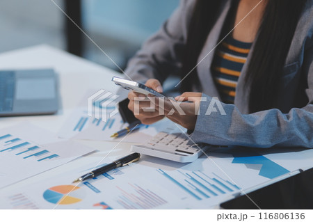 Attractive and cheerful millennial Asian businesswoman receiving a good message or email through her smartphone, sitting at her desk. Attractive and cheerful millennial Asian businesswoman receiving a good message or email through her smartphone, sitting at her desk. 116806136