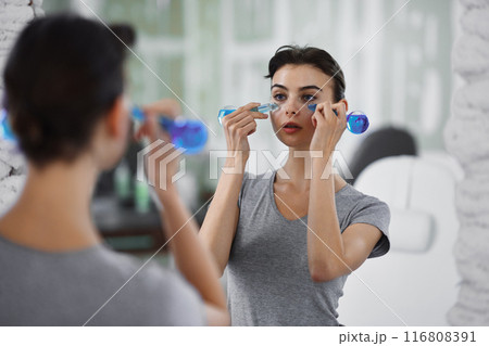 A young woman is doing a relaxing face massage using cold cryo spheres. A young woman is doing a relaxing face massage using cold cryo spheres. 116808391