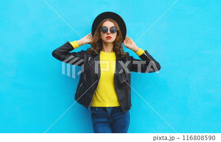 Fashion, trendy, stylish young woman in black hat, leather jacket, modern girl posing on blue 116808590