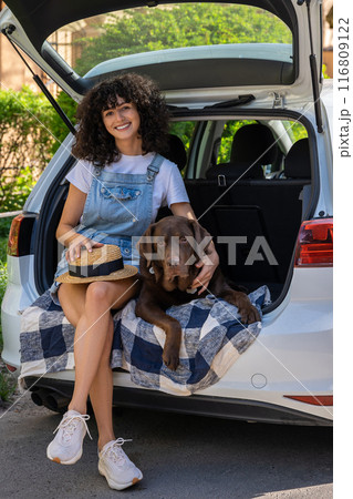 Cute curly-haired young woman sitting in the car with the dog ands looking happy Cute curly-haired young woman sitting in the car with the dog ands looking happy 116809122