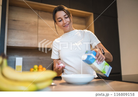 Young woman pouring milk while preparing breakfast 116809158