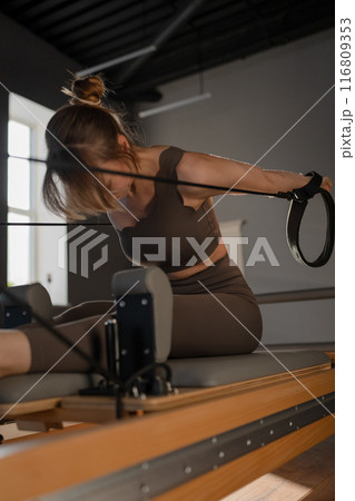 Woman training pilates on the reformer bed. Reformer pilates studio machine for fitness workouts in gym. Fit, healthy and strong authentical body. Fitness concept 116809353