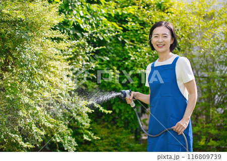 庭の緑に水やりをする笑顔のミドル女性 116809739