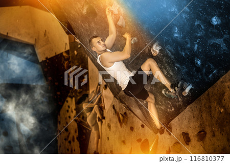 Young man climbing on artificial rock wall in rock-climbing gym 116810377