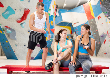 Three friends, man and woman, discuss their climbs on climbing wall without safety net, sitting on bench in recreation area Three friends, man and woman, discuss their climbs on climbing wall without safety net, sitting on bench in recreation area 116810513