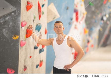 Young male climber posing at artificial rock wall in climbing hangar 116810575