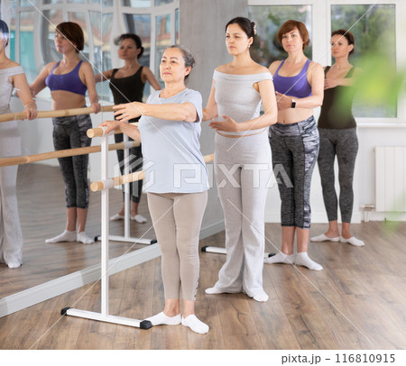 Elderly woman learning first ballet position at barre in group class Elderly woman learning first ballet position at barre in group class 116810915