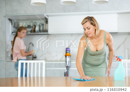 Blurry teen girl help mother doing housework in kitchen, mom cleaning dining table 116810942