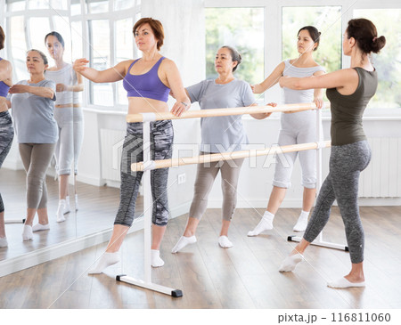 Woman mastering battement tendu with group of beginners and choreographer 116811060