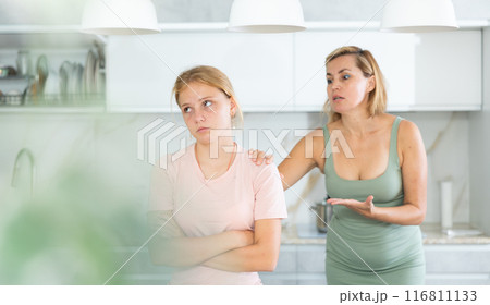 Offended teen girl listening to disapproving words of mother in home kitchen Offended teen girl listening to disapproving words of mother in home kitchen 116811133