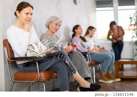 Young female employees sits in waiting room and waits for interview, holds resume documents Young female employees sits in waiting room and waits for interview, holds resume documents 116811146