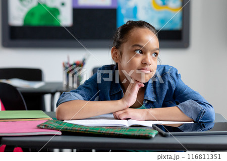 Bored biracial schoolgirl sitting at desk in class, leaning on hand, looking away, with copy space Bored biracial schoolgirl sitting at desk in class, leaning on hand, looking away, with copy space 116811351