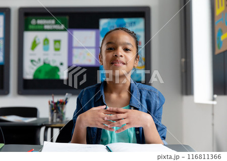Portrait of happy biracial schoolgirl sitting at desk in class, with copy space Portrait of happy biracial schoolgirl sitting at desk in class, with copy space 116811366