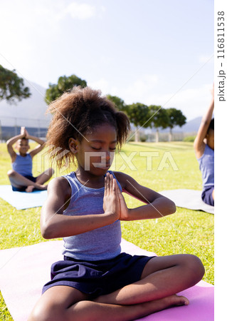 Happy african american schoolchildren doing yoga and meditating on field at school 116811538