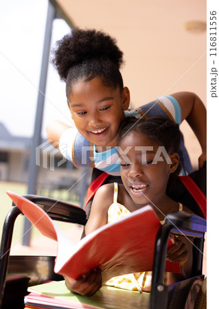Happy african american schoolgirl in wheelchair with her friend in corridor at school Happy african american schoolgirl in wheelchair with her friend in corridor at school 116811556