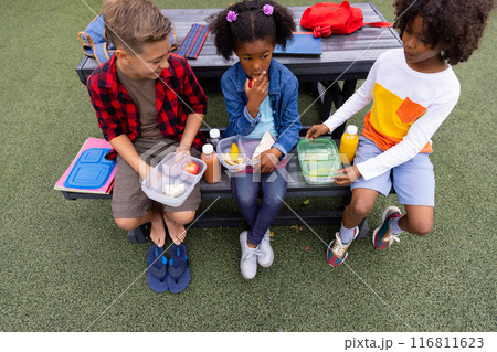 Happy diverse schoolchildren sitting at table and eating lunch at school 116811623