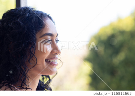 Smiling woman with curly hair looking out window, enjoying peaceful moment, copy space Smiling woman with curly hair looking out window, enjoying peaceful moment, copy space 116811663