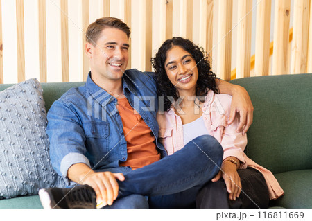 Smiling young couple sitting on couch, enjoying quality time together Smiling young couple sitting on couch, enjoying quality time together 116811669