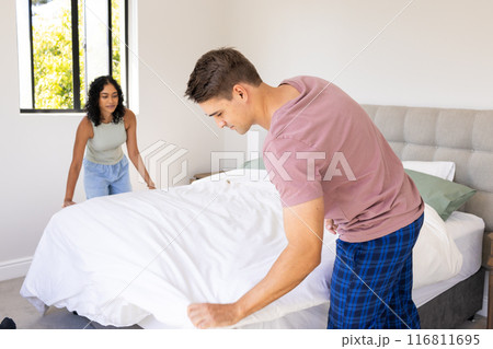 Making bed together, young couple tidying bedroom in morning routine Making bed together, young couple tidying bedroom in morning routine 116811695