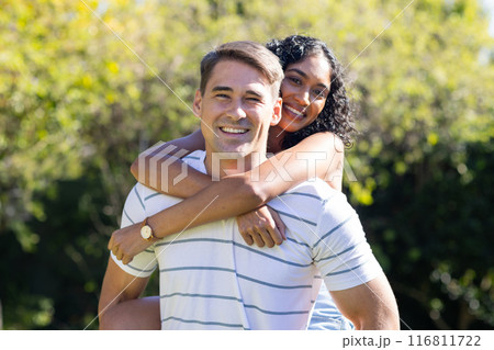 Smiling young couple enjoying piggyback ride outdoors in sunny park 116811722