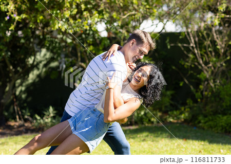 Young couple dancing and laughing together in sunny outdoor garden 116811733