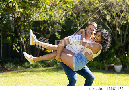 Man lifting and smiling with woman in backyard, enjoying playful moment together 116811734