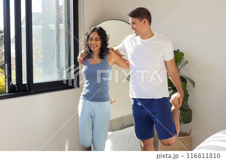 Stretching together, young couple enjoying morning exercise by window at home Stretching together, young couple enjoying morning exercise by window at home 116811810