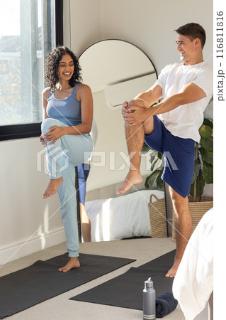 Practicing yoga together, young couple stretching on yoga mats in bedroom Practicing yoga together, young couple stretching on yoga mats in bedroom 116811816