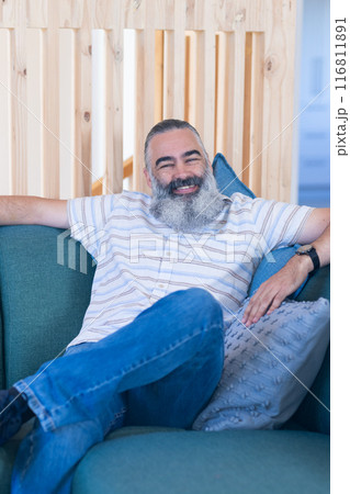 Smiling man with beard relaxing on couch, enjoying leisure time at home 116811891