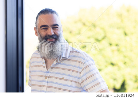Smiling senior man with gray beard standing outdoors in casual striped shirt 116811924