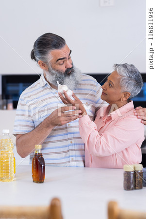 Senior couple in kitchen holding garlic and smiling at each other Senior couple in kitchen holding garlic and smiling at each other 116811936
