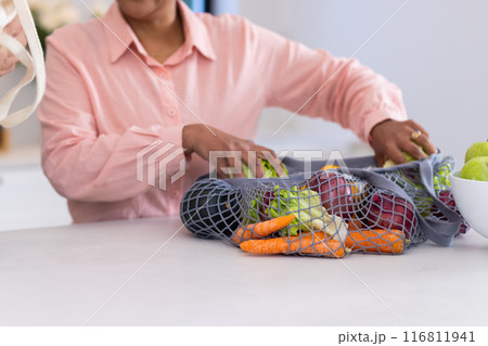 Unpacking fresh vegetables from reusable bag, person organizing groceries in kitchen 116811941