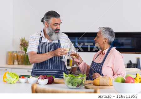 Senior couple toasting with wine glasses while preparing salad in kitchen 116811955