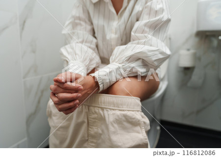 close up woman sitting on a toilet bowl in bathroom 116812086