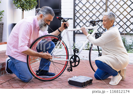 Repairing bicycle together, senior couple enjoying outdoor activity in courtyard 116812174