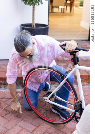 Repairing bicycle, senior man kneeling and fixing wheel outdoors Repairing bicycle, senior man kneeling and fixing wheel outdoors 116812193