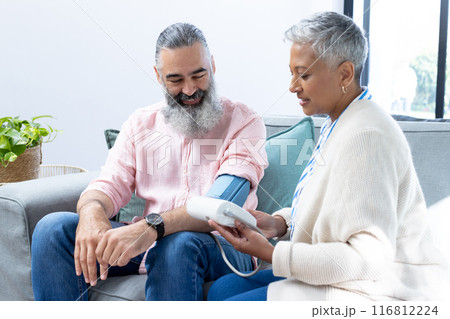 Checking blood pressure, woman using monitor on man sitting on couch 116812224