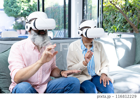 Senior couple using VR headsets, experiencing virtual reality at home 116812229