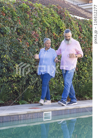 Senior couple walking by pool, holding coffee cups and enjoying conversation Senior couple walking by pool, holding coffee cups and enjoying conversation 116812277