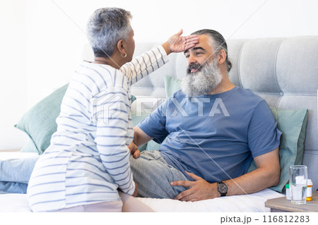 Checking temperature, woman caring for sick man in bed at home Checking temperature, woman caring for sick man in bed at home 116812283