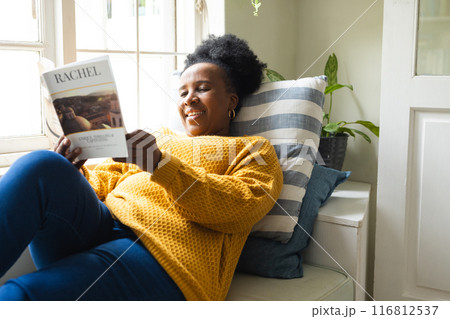 Happy senior african american woman lying on couch and reading book at home Happy senior african american woman lying on couch and reading book at home 116812537